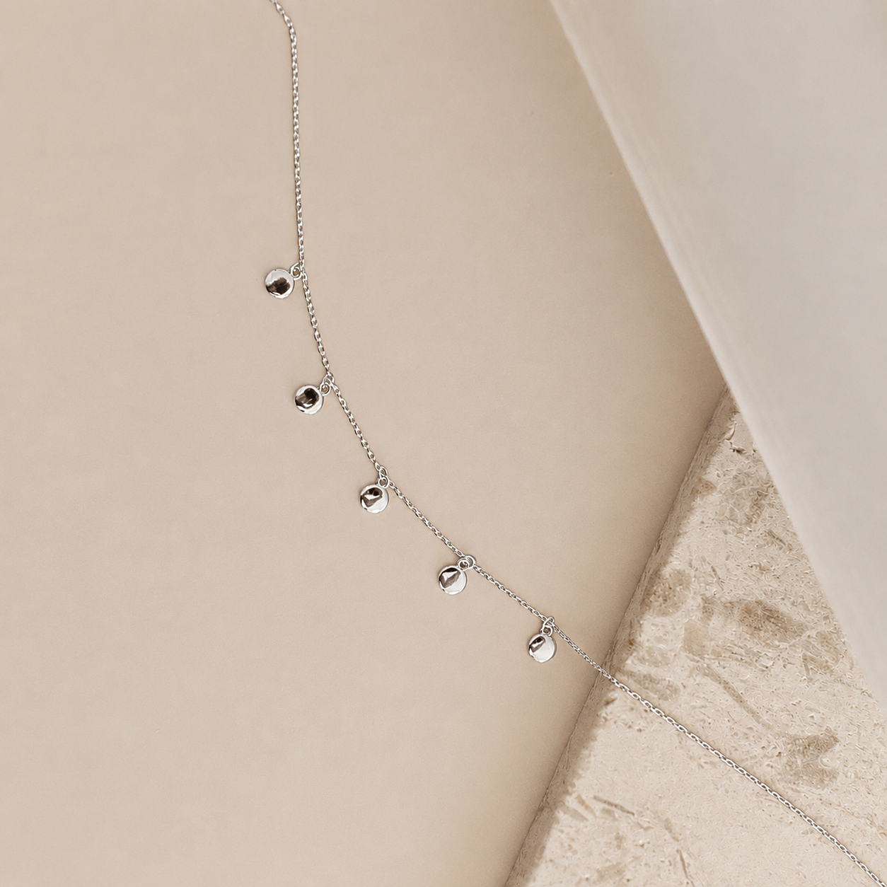 Silver necklace with small round pendants on a beige surface